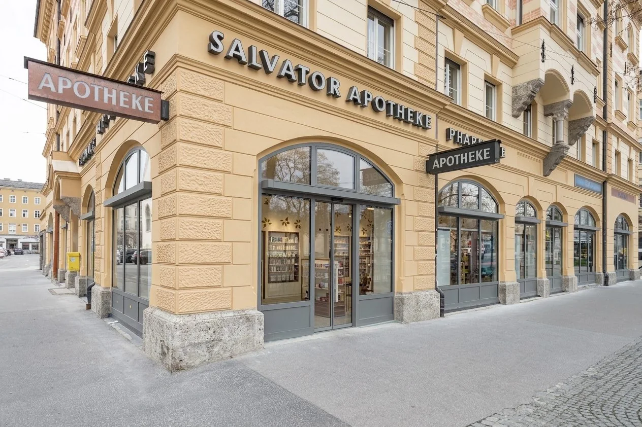 Eingang der Salvator Apotheke am Mirabellplatz 5: Eckhaus mit ockerfarbener Fassade, Rundbogenfenstern und Schriftzug